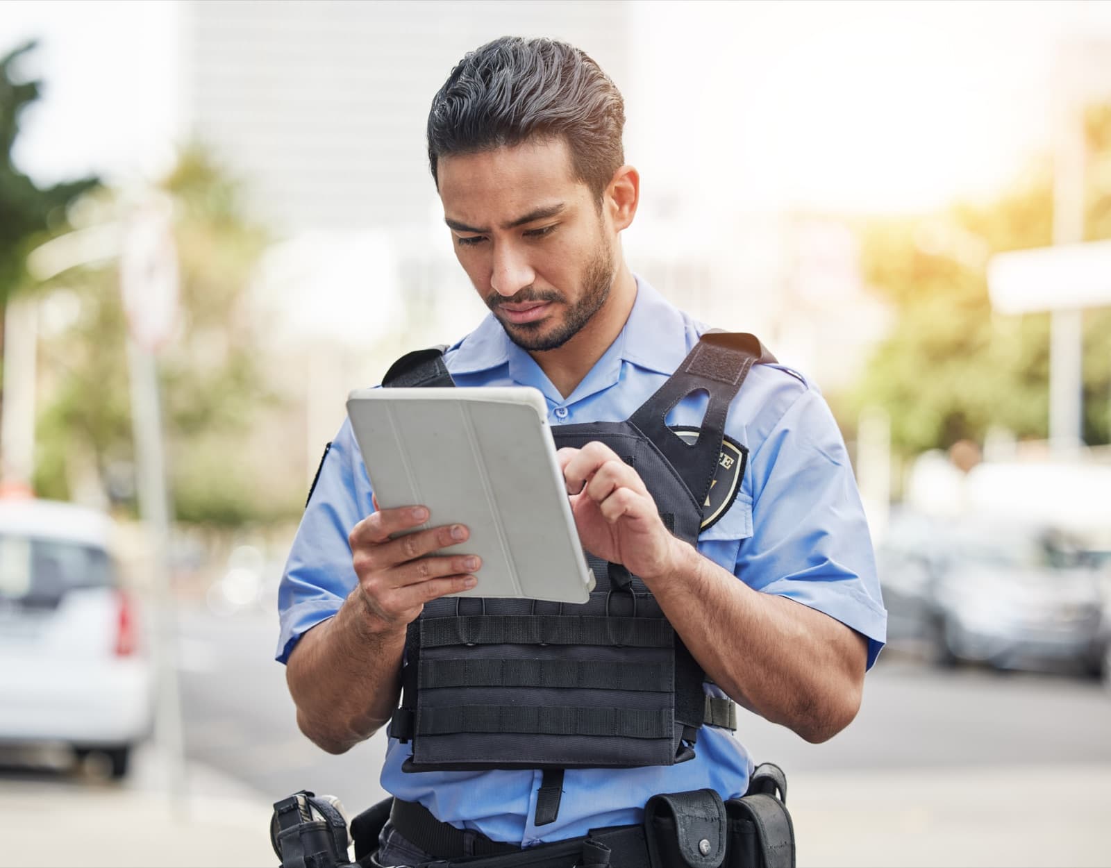 An officer on a street in daylight, making notes on a tablet held in both hands