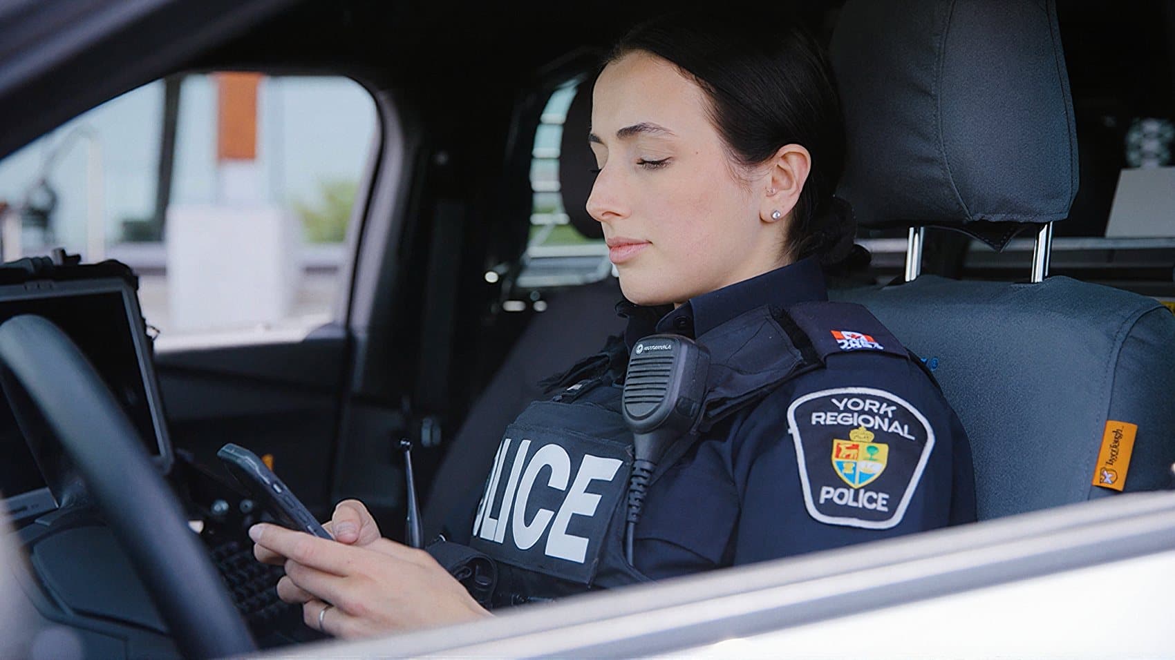 A York Regional Police officer using IMP eNotes on a handheld device in her cruiser, with the in-vehicle terminal beside her