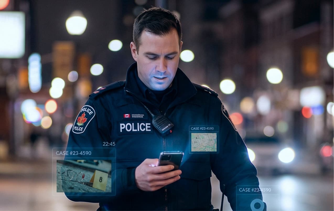 A police officer on a city street at night, writing up a call on his phone, with case cards beside him showing a scene photograph and a map