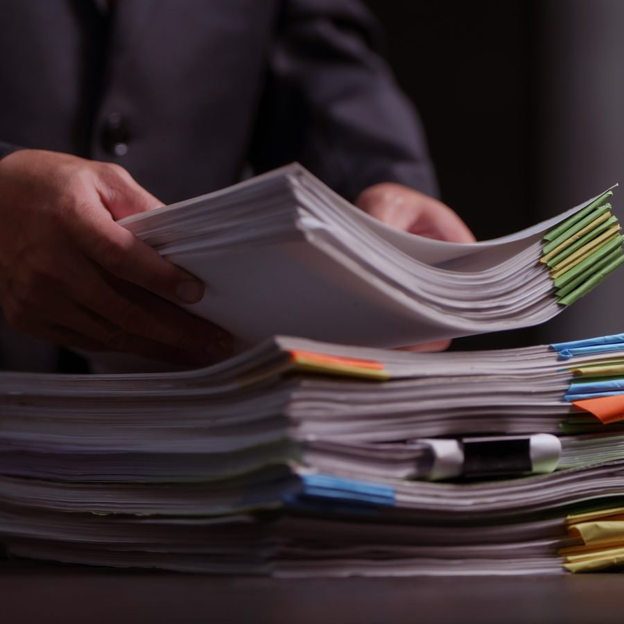 Hands lifting a sheaf of paper from two deep stacks of tabbed and indexed files on a desk